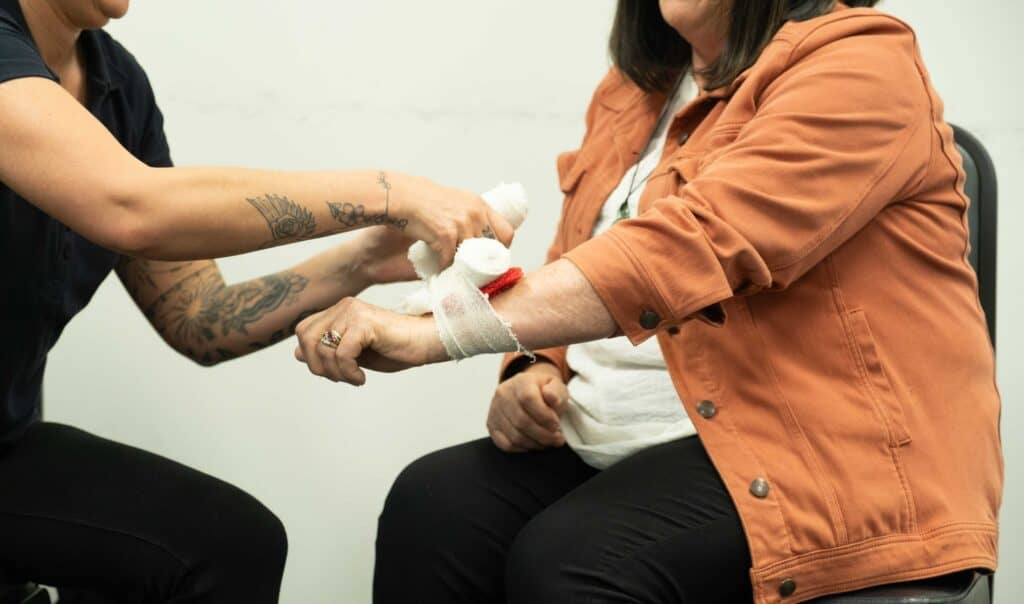 First aid training with a bandage being applied to a woman's arm during a Life Care session.