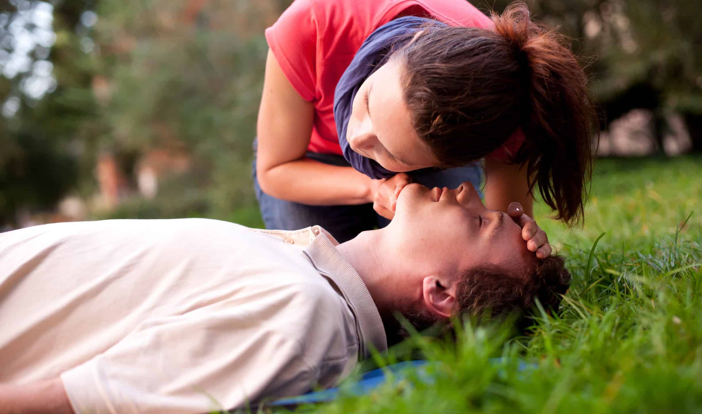 Woman performing CPR on an unconscious man during a first aid training session outdoors.